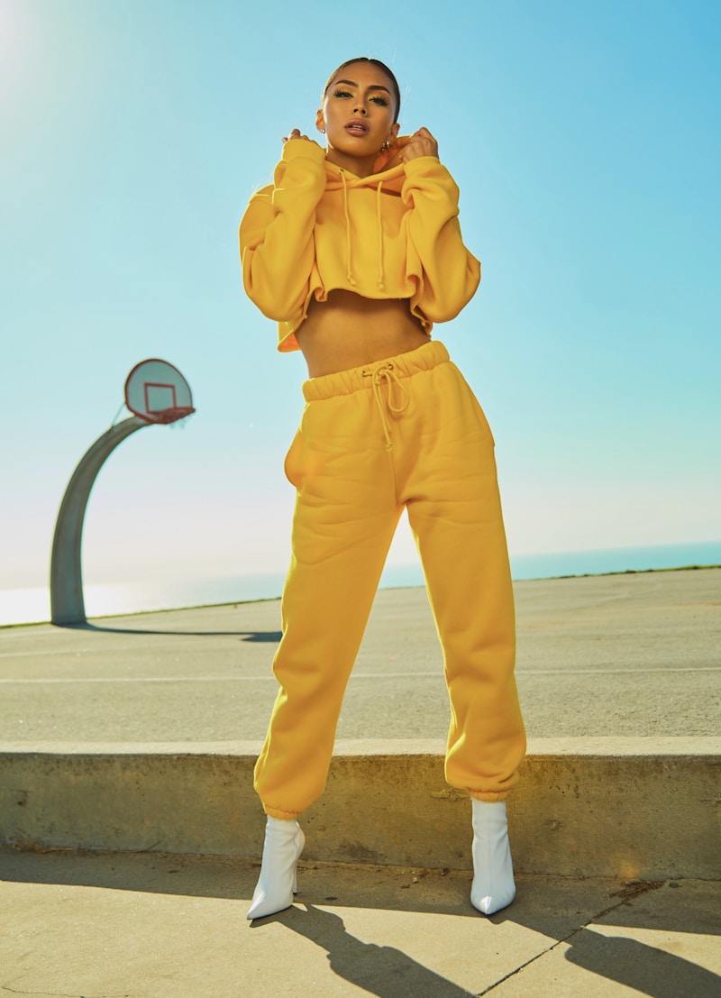 Source photo: woman in yellow hoodie on outdoor basketball court, dramatic collar-pull pose