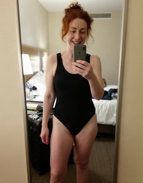 Source photo: a phone mirror selfie of a woman in her late thirties in a black one-piece swimsuit in a hotel room